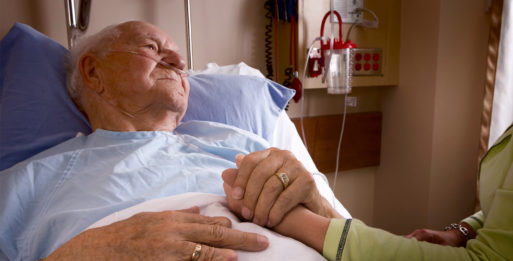 Elderly man in hospital bed holding someone else's hand representing palliative care