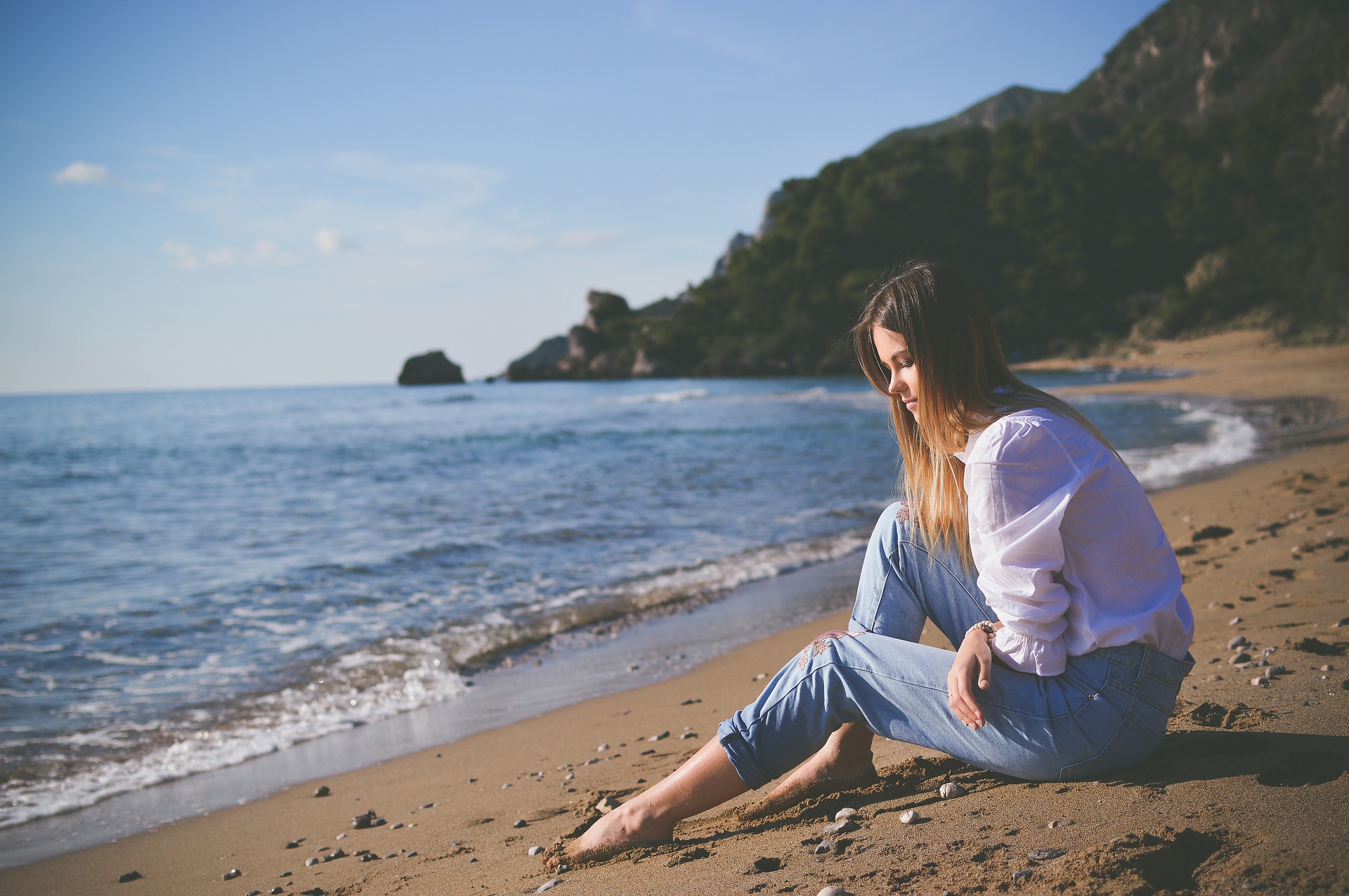 Woman sitting on a beach looking at the sand symbolizing grief