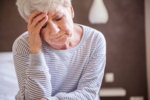 Elderly woman holding forehead and looking down showing frustration