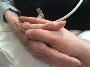 A son holds his elderly mother's hand; the last wishes of the dying often include spending time with loved ones
