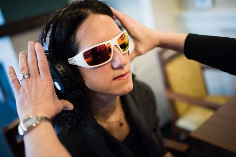Set of hands placing goggles and headphones onto a woman's head as part of the virtual dementia tour