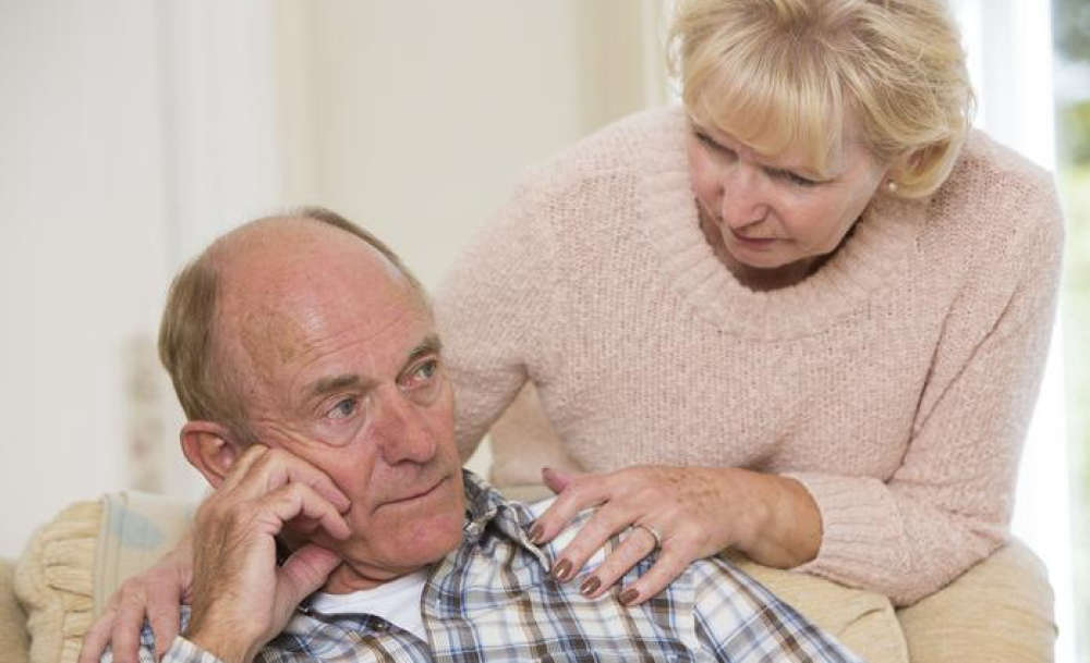 Elderly man sitting on couch while wife consoles him symbolizing mild cognitive impairment