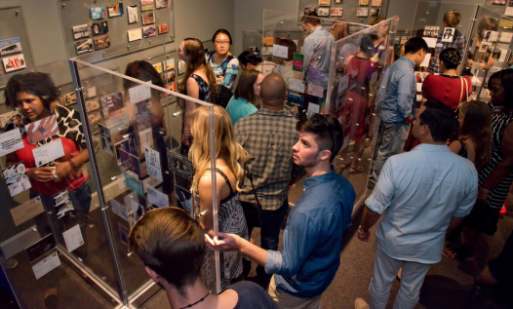 A group of people stand in a museum gallery filled with anonymous postcard confessions
