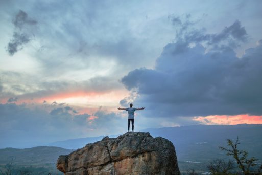 Man standing with arms wide open on a peak looking at sky