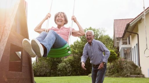 Elderly man pushing an elderly woman on a swing symbolizing playfulness and youth in old age.