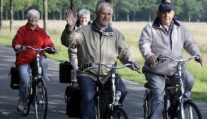 Group of four elderly people riding bicycles and exercising with one man waving at the camera