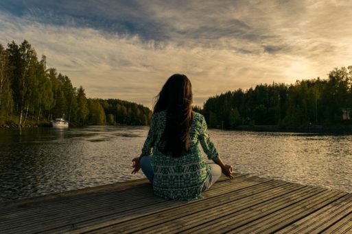 woman sitting in front of a lake meditating