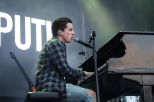 Photo of singer Charlie Puth on stage playing piano and singing into microphone.