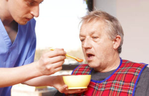 Man with late-stage dementia being fed by caregiver