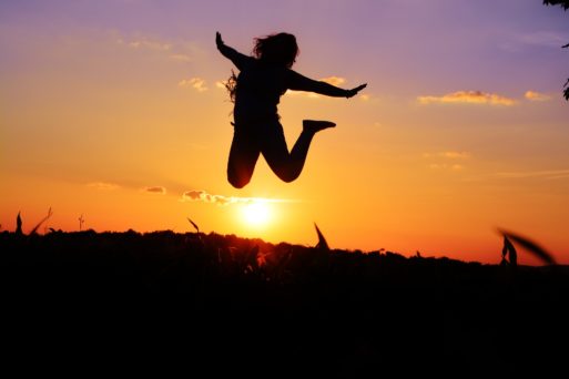 Silhouette of a woman jumping at sunset to signify life.
