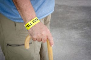 Elderly man holding a cane with wristband that reads "fall risk."