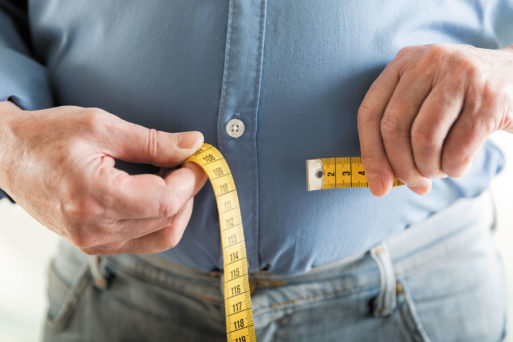 Man measuring stomach with a tape measure indicating that he is overweight