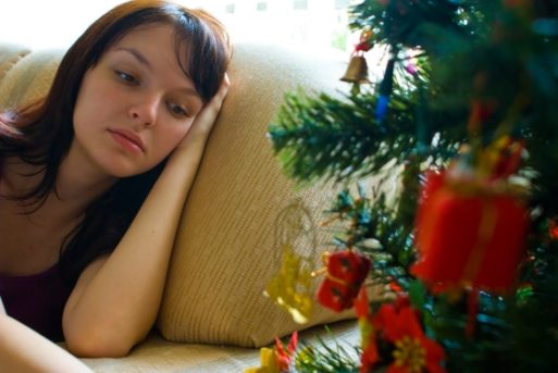Woman with the holiday blues resting on couch by Christmas tree