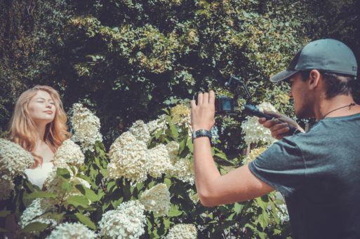 Man filming a woman in a garden.