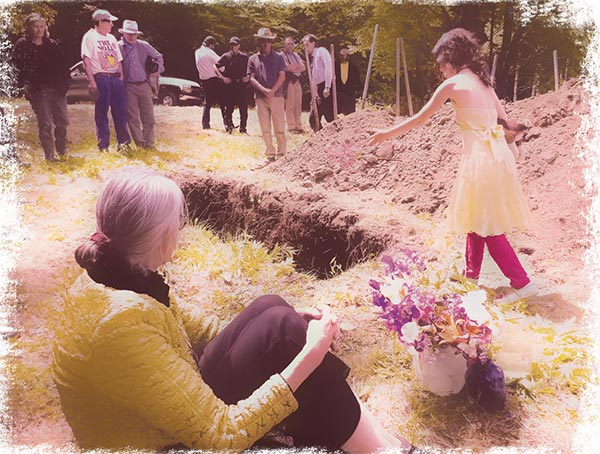 Group of people standing around a newly dug grave site.