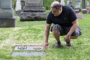 Elijah Shalis of the Michigan Society Sons of the American Revolution touches James Robinson's grave marker.