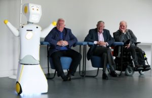 Three elderly men watching the Stevie II robot.
