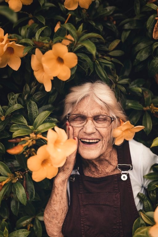 An elderly woman smiles with flowers, displaying the bravery often needed to embrace birth and death.