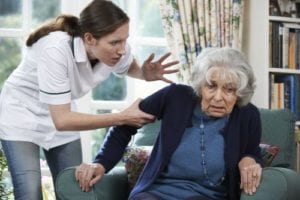 Health care worker grabbing arm of elderly woman indicating potential elder abuse.