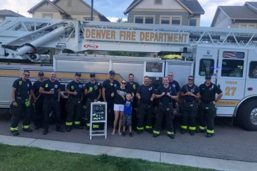 Brady Campbell and mother Amanda standing with firemen and lemonade stand sign.