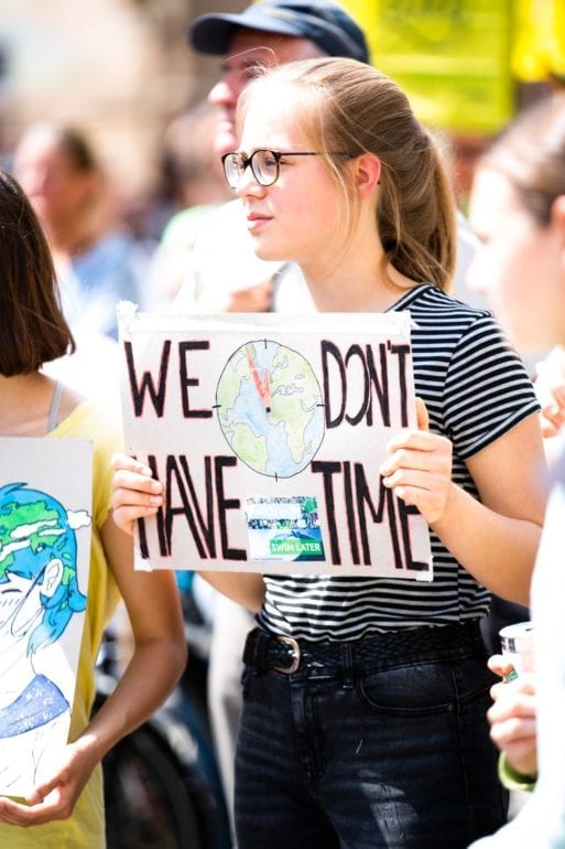 Young woman experiencing climate grief holds a sign reading, "We don't have time."
