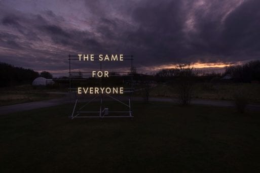 "The Same For Everyone" art installation illuminated against a dark sky.