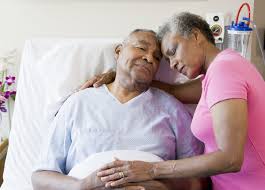 Female spousal caregiver hugging her husband who is laying in hospital bed.