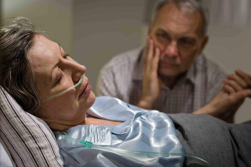 Male spousal caregiver sitting next to his sickly wife.