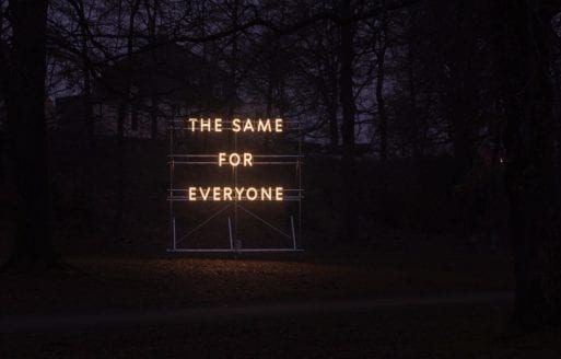 "The Same For Everyone" illuminated sign outside a tree grove.