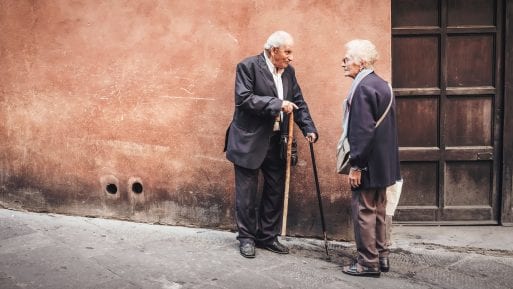 Two elderly people stand outside talking, making a connection 