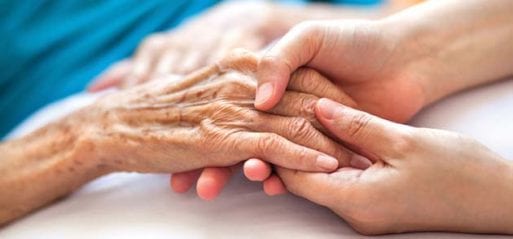 A hospice and palliative care health worker holding hands with a patient.