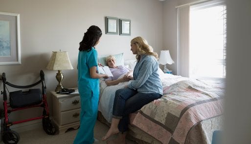 A nurse and family member talking with a woman receiving hospice and palliative care