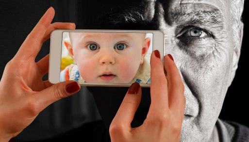 A baby's face while photographing an old man with a smartphone suggests leaving digital messages to loved ones.