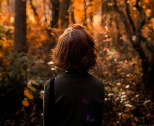 Woman stands among autumn leaves, recalling the quote by Robert Thurman about giving ourselves away before death.