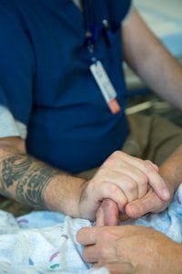 Jonathan Bartels holds a patient's hand as he helps them to navigate difficult questions and minimize the trauma of code blue deaths.
