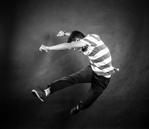 A man jumps in front of a grey background, exploring dance to cope with grief