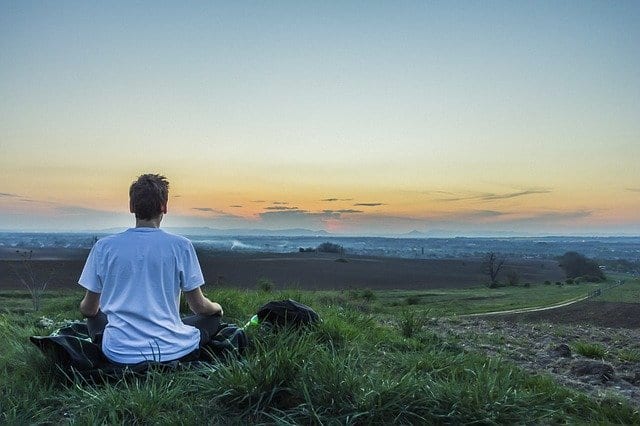 Man sits with his legs crossed, looking at the sunrise and living in the present moment