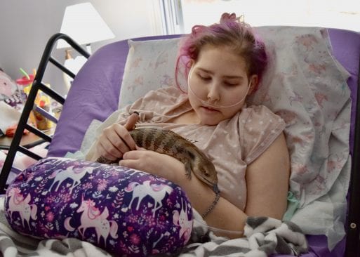 A young adult wish recipient with cancer holds a lizard in bed.
