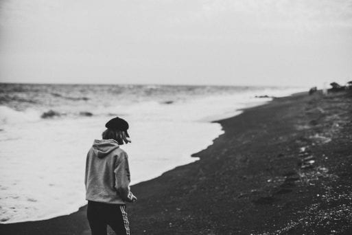 A woman walks along the beach in a black-and-white photo.