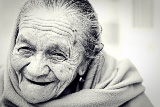 An elderly woman smiles at the camera in a black-and-white portrait.