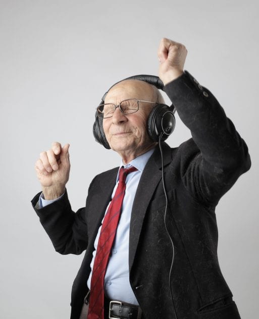 An elderly man in a suit dances while wearing headphones.