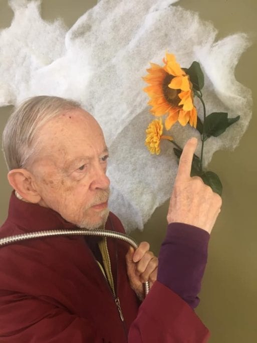 A senior man holds a sunflower in a recreation of "Self Portrait with a Sunflower."