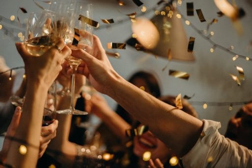 Hands reach up to toast glasses while gold confetti rains down.