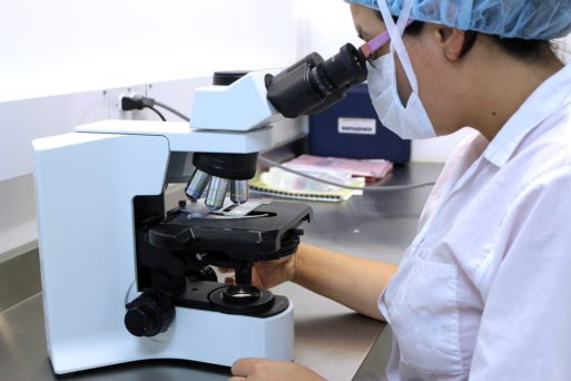 Scientist in mask and lab coat looking into microscope developing new Alzheimer's test
