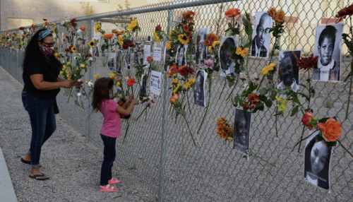 A child adds flowers to a Say Their Names Memorial with photos of victims on a fence