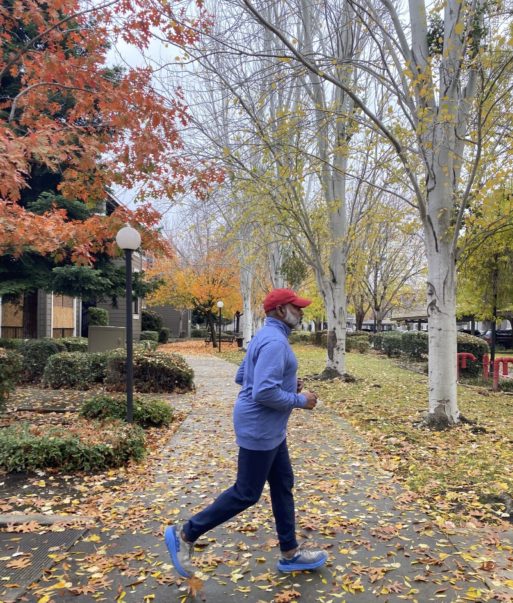 Les Aria jogging on the sidewalk in an autumn scene. Mr. Aria helps patients manage pain through mindfulness.