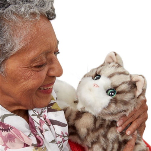 Older woman smiles at fuzzy robot cat used as a robot pet for older adults with dementia