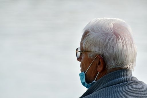 Elderly man with white hair facing away from camera and wearing a blue face mask pushed down grieves non-covid death