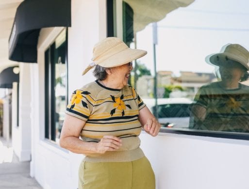 A woman experiencing old age looks at her reflection in a window.