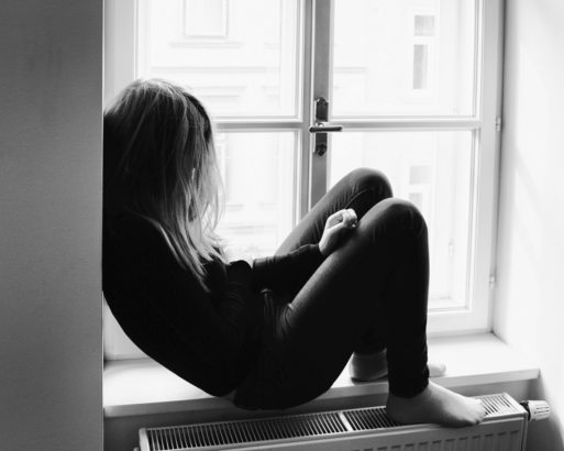 Young woman sitting in windowsill with her head down in black and white - decreasing life expectancy of young Americans